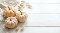 Three small decorative pumpkins in cream and peach tones arranged on white wooden surface with autumn leaves for seasonal home decor and fall crafting projects.