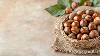 Fresh hazelnuts in rustic woven basket on burlap cloth against blurred beige background with green leaves, copy space for text. Natural food photography.