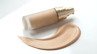 Luxury foundation bottle with golden pump dispenser and creamy beige makeup smear on white background for cosmetic advertising and beauty product marketing.