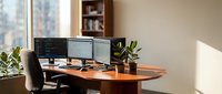 Modern home office workspace with dual monitor computer setup on wooden desk near window with natural light and indoor plants for productivity and remote work.