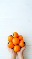 Hands holding fresh orange medlar fruits against white wooden background, isolated for design use on packaging, recipe blogs, healthy eating content, and culinary marketing materials.