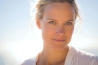 Young blonde Caucasian woman with natural makeup and gentle smile in soft golden sunlight for wellness and lifestyle content.