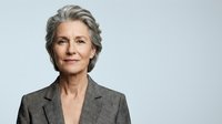 Mature woman with gray hair wearing professional gray blazer against neutral background, suitable for corporate, business, and leadership concepts.