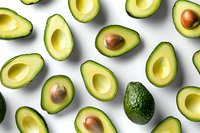 Fresh ripe avocado halves pattern on white background, organic healthy food layout with whole and cut fruits showing creamy flesh and brown pits.