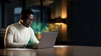 Young Asian businessman working late on laptop with digital holographic interface elements in modern office environment for technology presentations.
