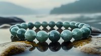 Green jade beaded bracelet with round polished stones reflecting on wet surface against blurred mountain landscape background at sunset.