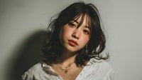 Young Asian woman with tousled medium-length hair and red lips wearing white lace top against neutral background, creating moody atmospheric portrait.