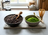 Coffee beans and matcha green tea powder in bowls on wooden board with traditional bamboo whisk and scoop in bright kitchen setting for beverage preparation.
