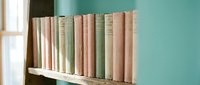 Row of vintage pastel books on a rustic wooden shelf against a soft teal wall, evoking nostalgia and cozy home library decor.