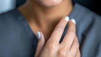 Young woman with light blue manicure touching neck in sensual gesture against dark background, soft focus beauty portrait highlighting feminine elegance and self-care.