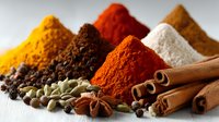Colorful heaps of aromatic spices including turmeric, paprika, and cinnamon sticks arranged on white wooden surface for cooking and seasoning dishes.