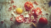 Raw egg yolk with broken shell pieces and fresh cut cherry tomatoes on rustic metal background, dramatic moody food photography with natural lighting.