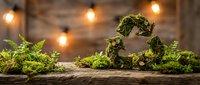 Moss-covered heart shape decoration with ferns on rustic wooden surface under warm string lights creating romantic botanical atmosphere for weddings.