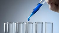 Laboratory pipette dropping blue liquid into test tubes for scientific research and chemical analysis experiments.