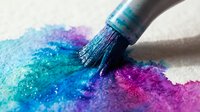 Paintbrush applying vibrant blue, purple, and pink watercolor pigments on white canvas, creating artistic gradient effect for creative projects and design inspiration.
