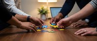 Business team collaborating with colorful puzzle pieces on wooden table in modern office environment for teamwork and problem-solving strategies.