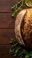 Artisan sourdough bread loaf with golden crust on rustic wooden table decorated with fresh oregano herbs for bakery and culinary cooking concepts.