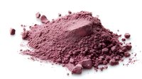 Pink cosmetic powder scattered on white surface, macro shot showing fine texture and loose particles of mineral makeup pigment for beauty products.