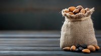 Rustic burlap sack filled with mixed nuts and dried plums on dark wooden table against blurred background, natural healthy snack concept for food packaging.