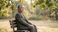 Senior Caucasian businessman in suit relaxing on park bench under autumn trees, enjoying peaceful moment outdoors during golden hour lighting.