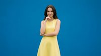 Young woman in yellow dress posing thoughtfully against bright blue background for fashion and lifestyle content.
