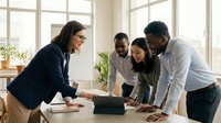 Diverse business team collaborating around laptop in bright modern office with large windows. Professional meeting with colleagues working together.