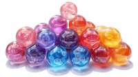 Colorful translucent glass beads in vibrant rainbow hues arranged in pyramid formation, showcasing light reflection and transparency on white background.