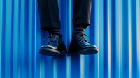 Levitating black leather shoes against vibrant blue striped background, creating surreal floating effect for creative commercial and fashion concepts.