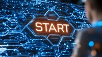 Glowing orange start button on futuristic blue digital interface with hexagonal pattern and circuit design elements. Business professional viewing interactive display.