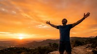 Man with arms raised celebrating success at sunrise over mountain landscape with golden sky.