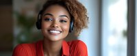 Young African American woman with natural curly hair wearing red blouse and wireless headphones smiles confidently while listening to music or audio content.