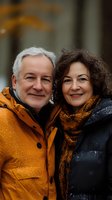 Happy mature couple in winter clothing smiling outdoors during autumn season. Gray-haired man in yellow jacket and brunette woman in black coat with orange scarf.