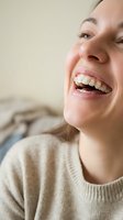 Young woman with ceramic braces smiling happily showing orthodontic treatment results in cozy sweater for dental care and oral health concepts.