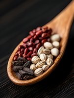 Wooden spoon filled with red kidney beans, white pistachios and dried dates on dark background, macro food photography for healthy eating and cooking concepts.