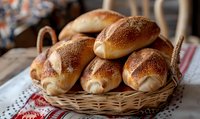 Fresh homemade bread rolls with golden crust and sesame seeds served in rustic wicker basket on traditional linen cloth. Close up view of artisanal baking.