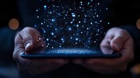 Hands holding digital tablet with magical blue glowing particles rising up against dark background, creating mystical technology concept.