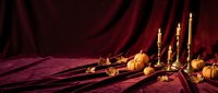 Elegant autumn still life with pumpkins, candles and rich burgundy velvet drapery creating warm atmospheric lighting for seasonal decor and harvest themes.