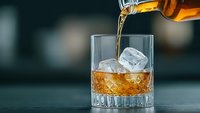 Whiskey being poured from bottle into crystal glass with ice cubes on dark surface creating elegant drinking scene for bar and restaurant concepts.