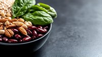 Mixed legumes and fresh spinach leaves in black ceramic bowl on dark background, healthy protein food source for vegetarian and vegan nutrition.