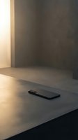 Black smartphone lying on concrete surface in modern minimalist interior with warm natural light casting shadows on dark walls.