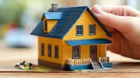 Yellow suburban house model with blue roof and porch, miniature architectural display on wooden surface showing residential property details for real estate presentation.