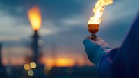Burning torch held in gloved hand against dramatic sunset sky with bokeh lights and cityscape silhouette in background creates atmospheric mood.