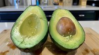 Fresh ripe avocado cut in half showing creamy green flesh and brown pit on wooden cutting board, close up view of raw organic produce.