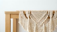 Handmade macrame wall hanging draped over a wooden table, featuring intricate knotted patterns and fringe tassels in natural cotton.