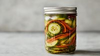 Fresh cucumber and carrot pickles in mason jar with herbs and spices, homemade fermented vegetables on rustic background, selective focus.