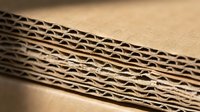 Corrugated cardboard sheets stacked showing detailed fluted structure and brown kraft paper layers for packaging and shipping applications.