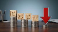 Wooden blocks spelling COST on decreasing coin stacks with red arrow showing downward trend, representing budget reduction and expense management strategies.