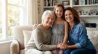 Three generations of Caucasian women smiling together on a sofa at home, grandmother, mother and granddaughter bonding in a bright living room.