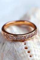 Rose gold wedding band with sparkling diamonds resting on white seashell in soft natural lighting, elegant jewelry photography for bridal collections.
