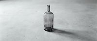 Empty glass bottle on concrete surface casting shadow, monochrome still life composition for beverage, alcohol, or recycling concepts.